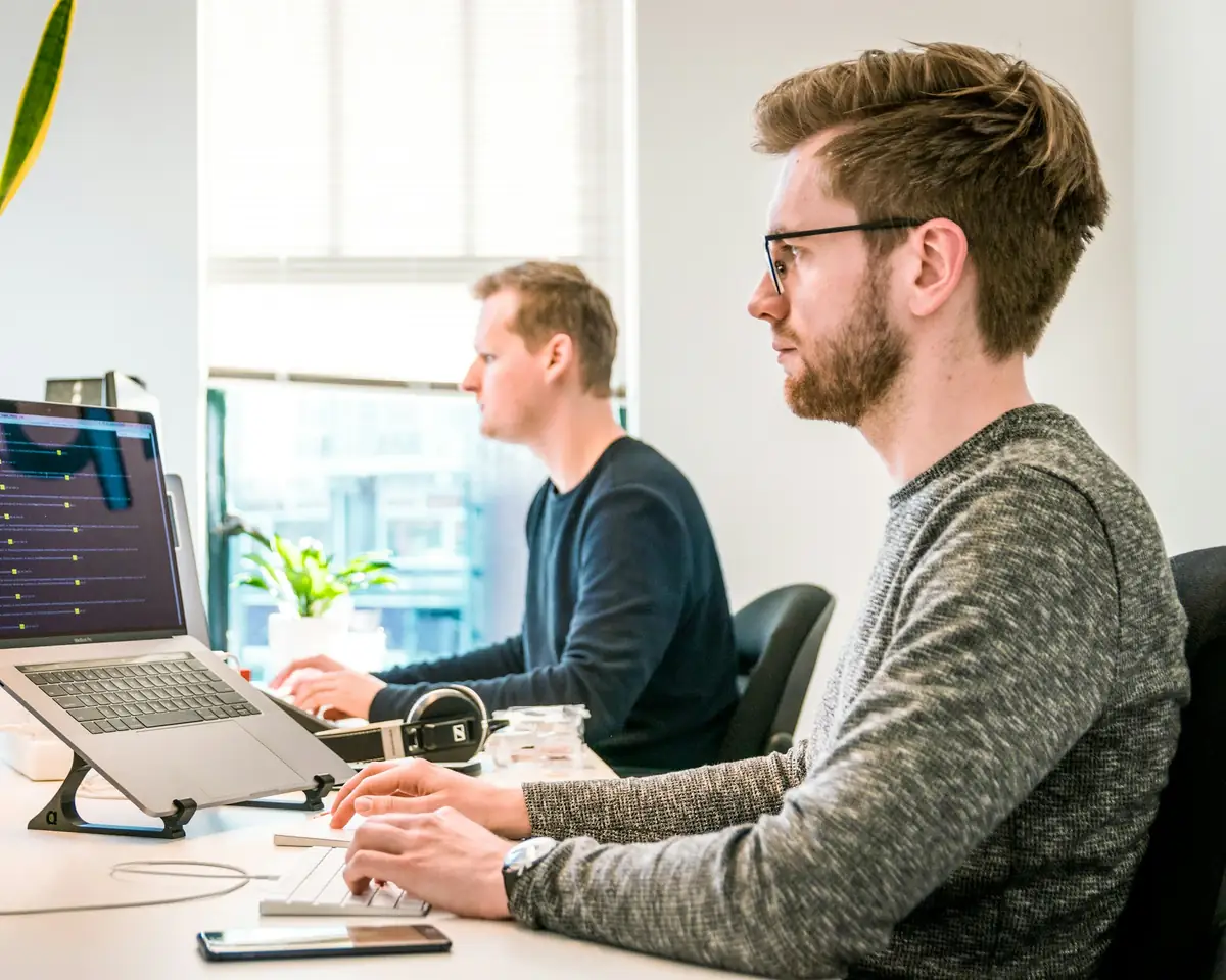 Twee mensen aan het werk achter een laptop en beeldscherm in een licht kantoor