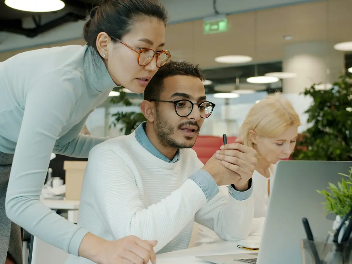 Drie mensen bespreken samen iets op een laptop in een modern kantoor